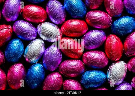 A portrait of a lot of delicious chocolate easter eggs wrapped in colorful tin foil. There are red, blue, white, purple and pink eggs all with their o Stock Photo