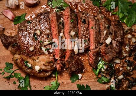 Freshly seared medium rare sirloin steak on the chopping board basted in butter, garlic, shallot and parsley Stock Photo