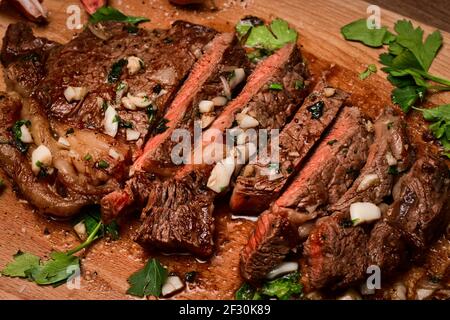 Freshly seared medium rare sirloin steak on the chopping board basted in butter, garlic, shallot and parsley Stock Photo