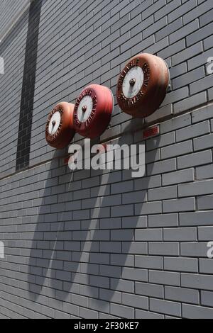 Closeup of three red fire sprinkler alarms mounted on a grey brick wall