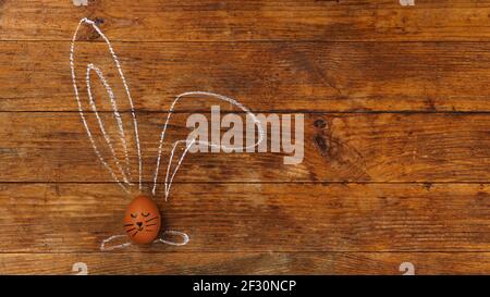 Egg on a wooden background. Chalk-drawn ears and a painted muzzle. Top view Stock Photo