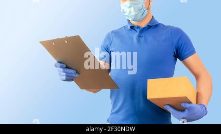 Delivery man in blue  t-shirt uniform sterile face mask gloves  with cardboard boxes and tablet in hand isolated on blue background. Guy employee work Stock Photo