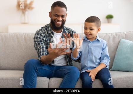 Black Father And Son Making Video Call Using Smartphone Indoor Stock Photo