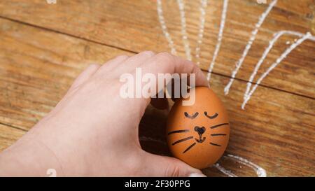 A female hand holds an egg with a cute face. The ears are drawn with chalk Stock Photo