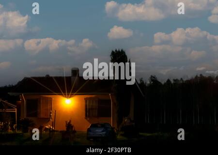 A yellow house in darkness against a blue sky with white clouds in the countryside Stock Photo