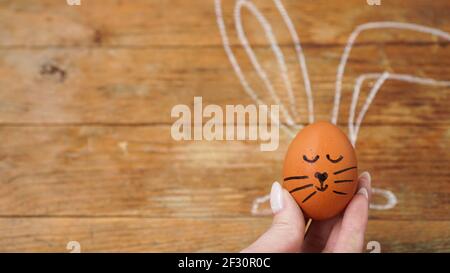 A female hand holds an egg with a cute face. The ears are drawn with chalk Stock Photo