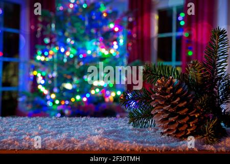 Fir cone on white snow isolated on blur Christmas tree lights background. Stock Photo
