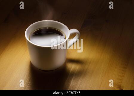 Cup of coffee under a spotlight and on a wooden ground. Stock Photo