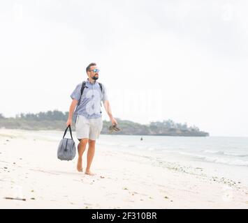 Cheerful adult man with bag having fun on tropical beach Stock Photo