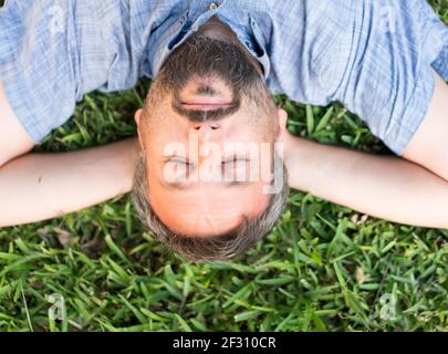 Adult caucasian man lying upside down portrait on grass meadow Stock Photo