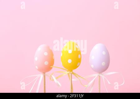 Colorful Easter eggs on sticks on pink background. Festive Easter holiday greeting card with copy space. Stock Photo