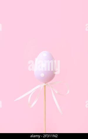 Lilac Easter egg on stick on pink background. Festive Easter holiday greeting card with copy space. Stock Photo