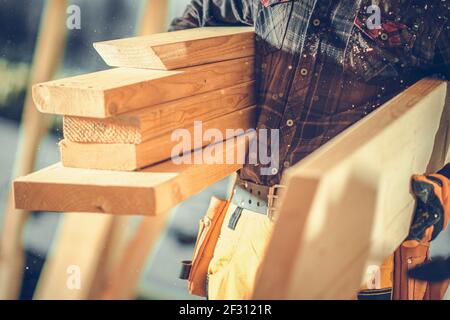 Construction Worker Moving Pieces of Wood Beams in Construction Zone. Close Up Photo. Industrial Theme. Stock Photo