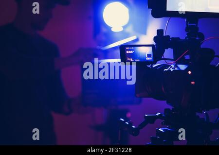 Documentary Film Stage in Blue Illumination. Professional Film Lighting and Digital Cinema Camera. Film Crew in Front of Camera with Movie Clapper in Stock Photo