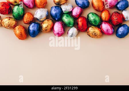 Easter chocolate mini eggs wrapped in a colorful foil, scattered on a beige background, top view, copy space. Stock Photo