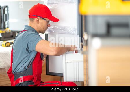 Caucasian RV Center Technician in His 40s Replacing or Repair Broken Motorhome Refrigerator. RVing Theme Stock Photo