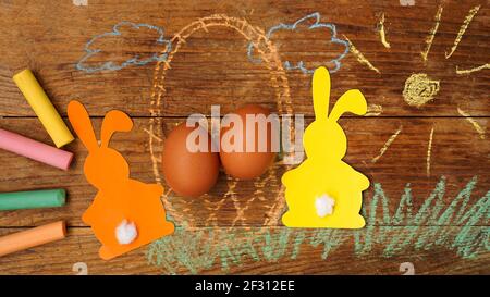 Two Easter bunnies made of paper and eggs in a basket. Drawn with chalk Stock Photo