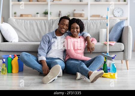 Tired black couple sitting on floor with cleaning tools Stock Photo