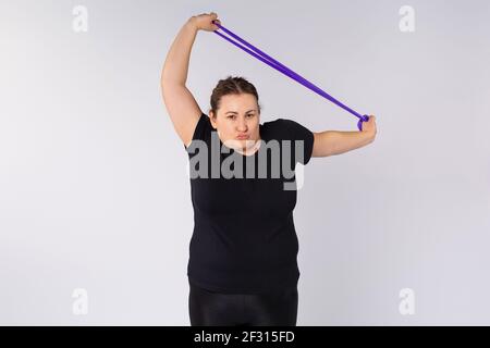 Aerobics pilates large woman with rubber elastic band in a row at fitness gym. Grey background and plus size woman practicing sport. Healthy diet Stock Photo