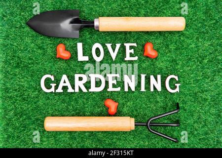 Lettering LOVE GARDENING with garden hand tools and hearts on green grass Stock Photo