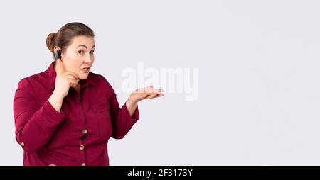 Banner- long format. Body positive female customer services agent with headset in call center. Large woman showing empty hand to side blank space for Stock Photo