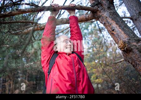 Active senior woman happy hanging from tree in forest Stock Photo
