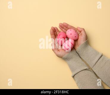Female hand holding multicolored decorative easter eggs on a beige background, top view Stock Photo