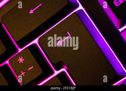 Macro closeup of pink purple illuminated return key on computer keyboard (focus on return sign) Stock Photo