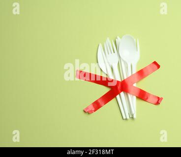 Plastic forks and spoons glued with red tape on a green background, avoiding plastic Stock Photo