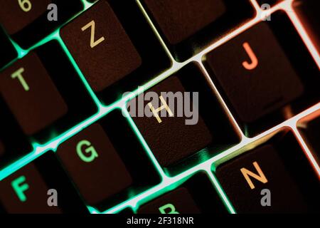 Macro closeup of green yellow illuminated keys of computer keyboard (focus on letter H) Stock Photo