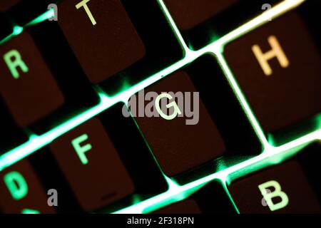 Macro closeup of green yellow illuminated keys of computer keyboard (focus on letter G) Stock Photo