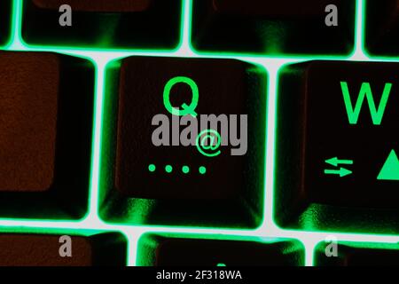 Macro closeup of isolated green illuminated key with letter Q and at sign on computer keyboard (focus on blurred at symbol) Stock Photo