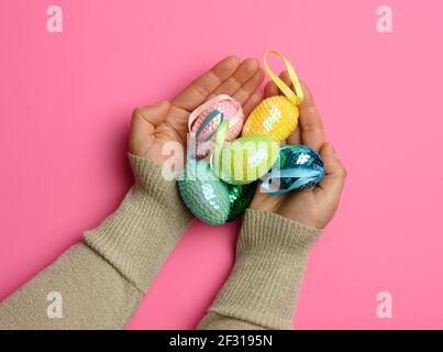 Female hand holding multicolored decorative easter eggs on pink background Stock Photo
