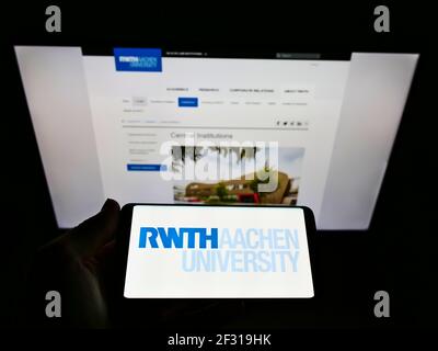 Person holding smartphone with logo of German education institution RWTH Aachen University on screen in front of webpage. Focus on phone display. Stock Photo