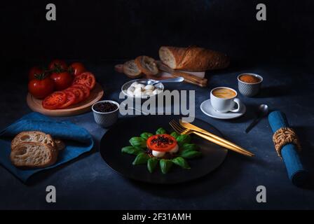 Variation of Caprese salad, slices of fresh ripe tomato, mini mozzarella, leaves of fresh basil and balsamic caviar. Dark background table. Stock Photo