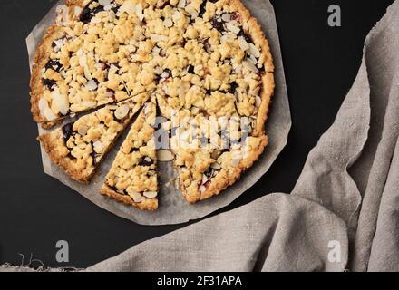 Baked round crumble pie with plum cut into pieces on a black background Stock Photo