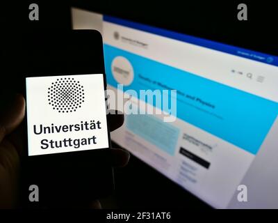 Person holding cellphone with logo of German education institution University of Stuttgart on screen in front of webpage. Focus on phone display. Stock Photo