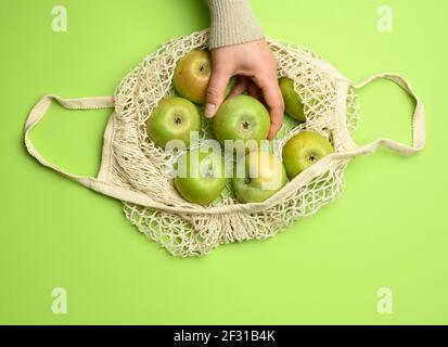Beige textile bag with green apples on a green background, the concept of reusable things Stock Photo