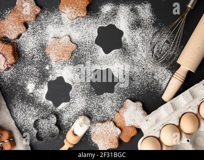 Baked star-shaped gingerbread cookie sprinkled with powdered sugar on a black table and ingredients Stock Photo