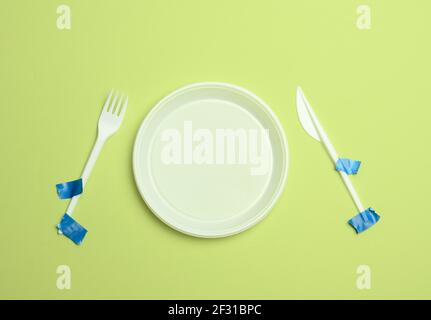 Disposable plastic forks and spoons glued with blue tape on a green background, avoiding plastic, preserving the environment Stock Photo