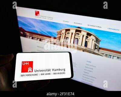 Person holding cellphone with logo of German education institution Universität Hamburg (UHH) on screen in front of web page. Focus on phone display. Stock Photo