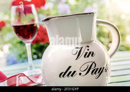 Vin du Pays table wine jug and glass of simple French country red wine on holiday alfresco terrace table with floral garden sunset Gites de France Stock Photo