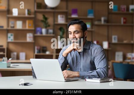Bearded indian business man watching online webinar on laptop computer. Stock Photo