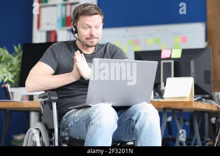 Man in wheelchair and wearing headphones with microphone works on laptop Stock Photo