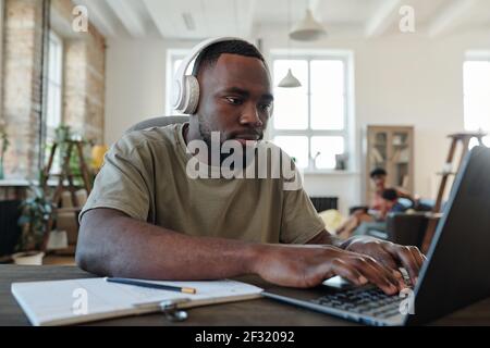 Young creative male designer in headphones pressing laptop buttons while working over new online project or presentation in home environment Stock Photo