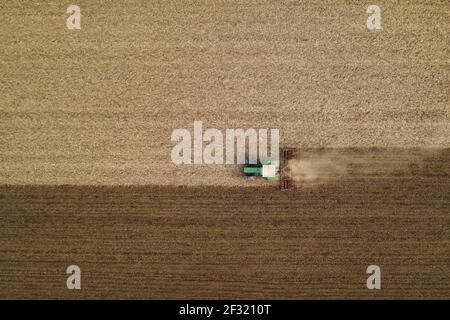 Aerial view of agricultural tractor tilling and harrowing ploughed field, directly above drone pov image of machinery working on farmland Stock Photo