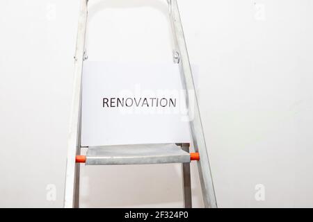 text renovation on white paper.metal stepladder for renovation work against a white plastered wall. Home repair concept. place for text.Stepladder Stock Photo