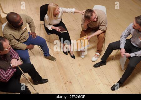 Blond mature female psychologist touching shoulder of young bearded man while comforting him and giving advice about his problem Stock Photo