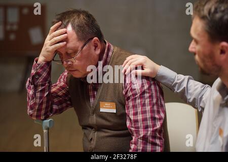 Troubled mature male in casualwear and eyeglasses touching head while thinking of his problems, confident young man comforting him Stock Photo