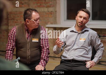 Confident male psychologist in smart casualwear pointing out and describing the main facets of problem being discussed at session Stock Photo